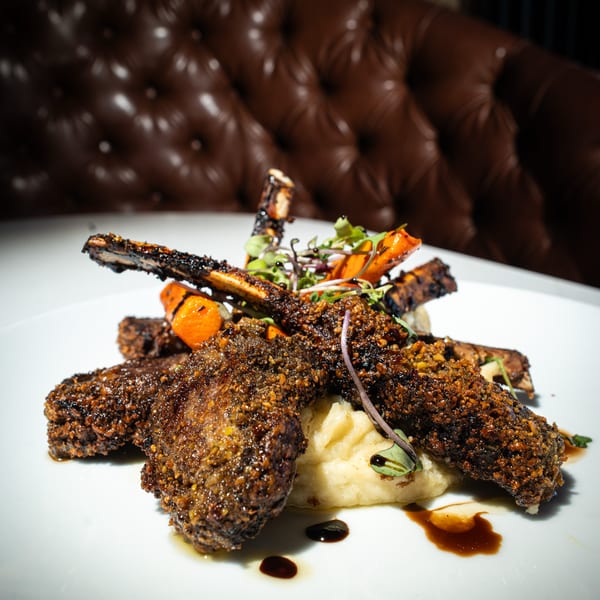 Crispy lamb chops with mashed potatoes, roasted carrots, and microgreens on a white plate.