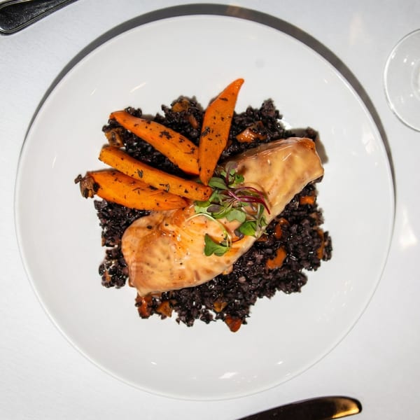 Salmon fillet with black rice, roasted carrots, and microgreens on a white plate.