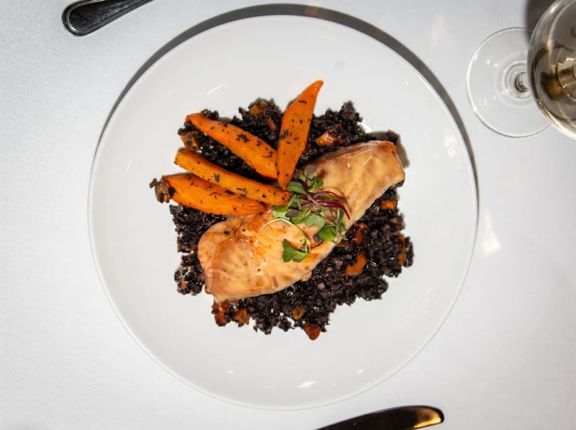 Salmon fillet with black rice, roasted carrots, and microgreens on a white plate.