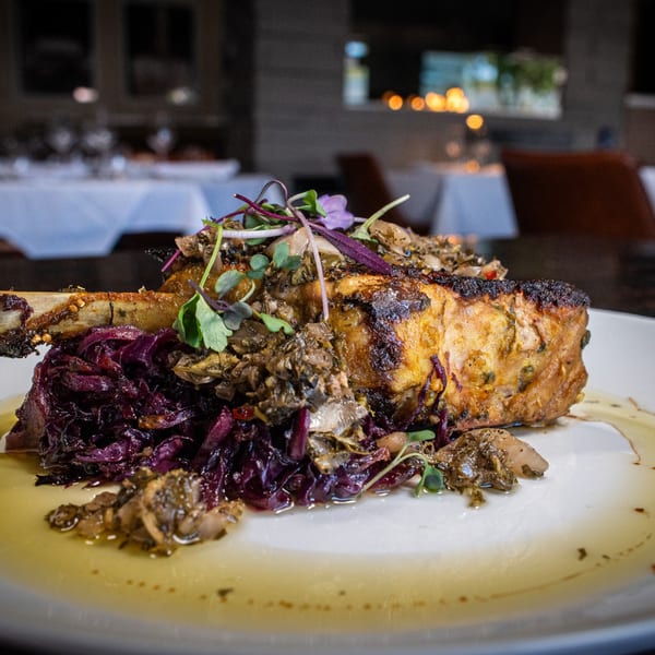 Pork chop with bone, red cabbage, and mushrooms on a white plate in a restaurant setting.