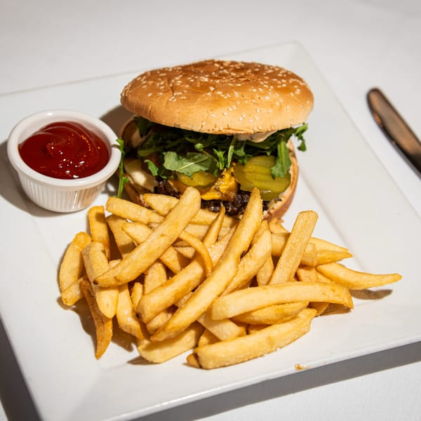 A gourmet burger with arugula, pickles, and cheese, served with golden fries and ketchup on a white plate.