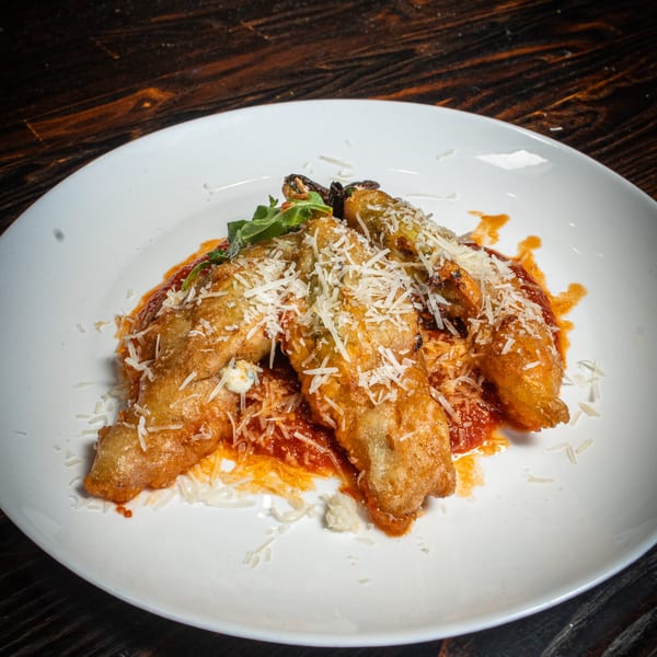 Fried zucchini blossoms with tomato sauce, grated cheese, and basil on a white plate.