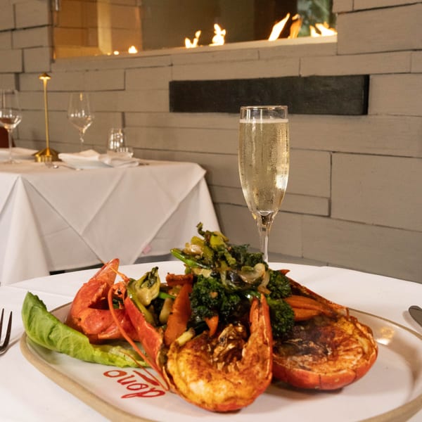 Lobster and vegetables on a plate with a glass of champagne, in a restaurant with a fireplace.
